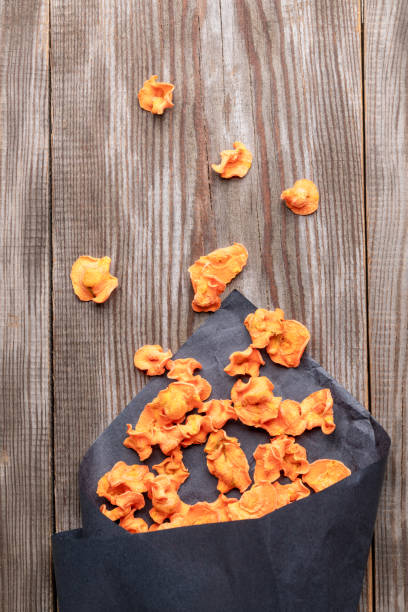 pomarańczowe zdrowe chipsy marchewkowe spadające z czarnej papierowej torby na stary drewniany stół. - root paper black textured zdjęcia i obrazy z banku zdjęć