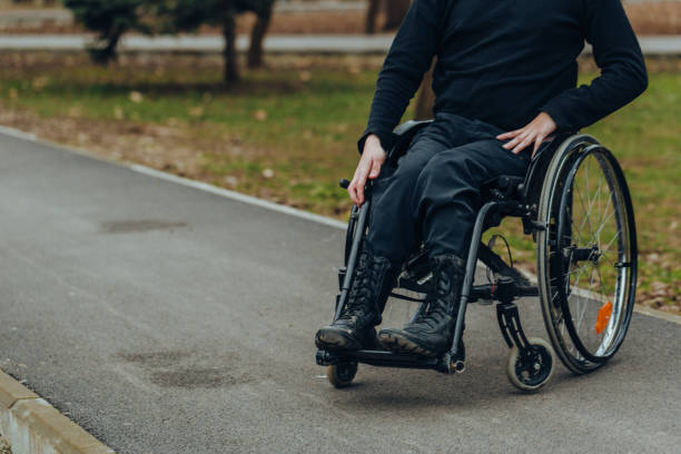 close-up de mano masculina en la rueda de silla de ruedas durante el paseo en el parque. tiene las manos en el volante. - parálisis fotografías e imágenes de stock