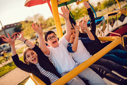 Group of children enjoying on a spinning ride in amusement park with arms raised