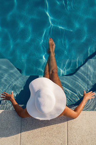Sexy photo model with a bright hat sitting relaxed in the pool photographed from above