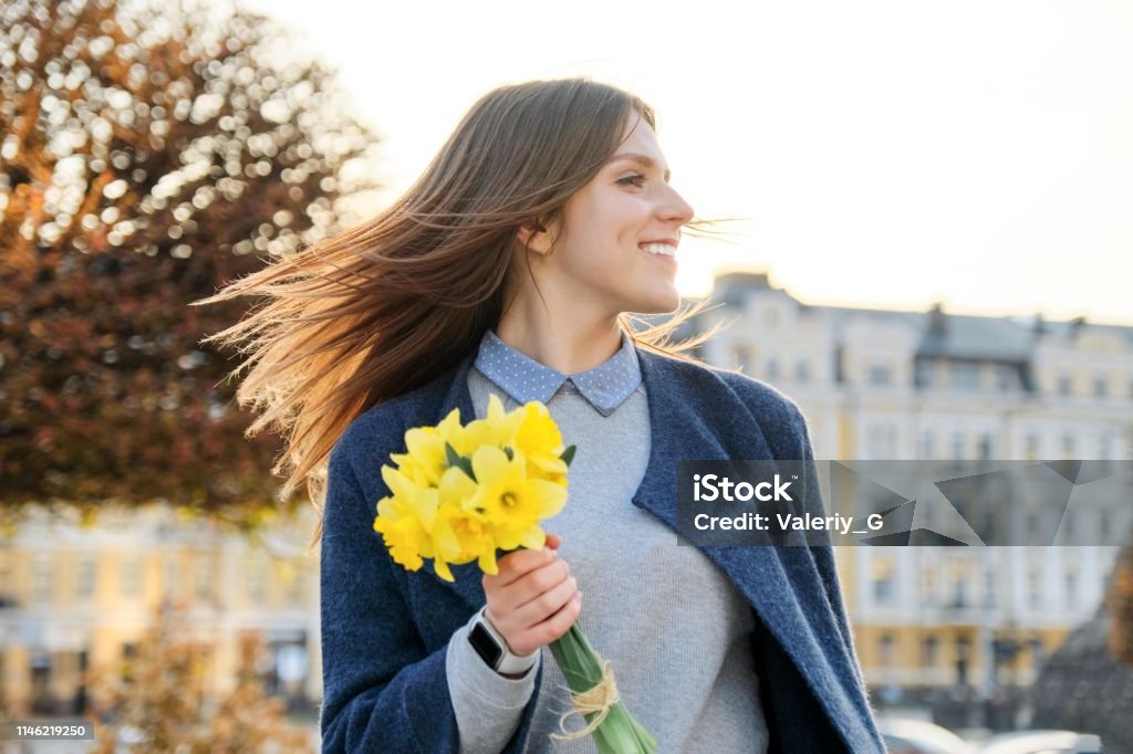 Outdoor portrait of young beautiful girl with bouquet of yellow spring flowers, background city street, architecture Outdoor portrait of young beautiful girl with bouquet of yellow spring flowers, background city street, architecture. Daffodil Stock Photo