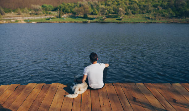 istock Anonymous man with dog sitting on pier 1146224519