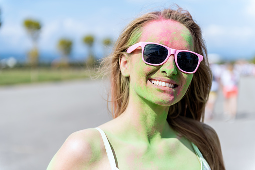 Cute woman covered in face powder on holi color festival smiling at camera and enjoying the color event.