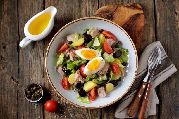 French salad Nicoise with tuna, boiled potatoes, egg, green beans, tomatoes, dried olives, lettuce and anchovies. Top View. stock photo
