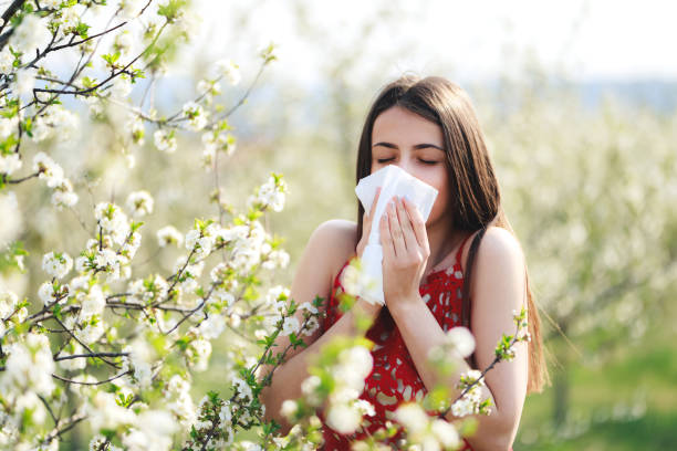 Blowing nose in blossoming garden Allergy season, young woman blowing her nose and sneezing in blossoming garden. hayfever stock pictures, royalty-free photos & images
