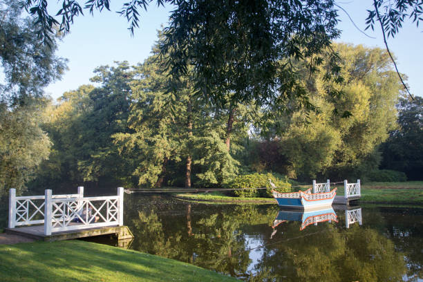 Park with romantic lake and boat tied up to a jetty. Summer time with green trees. Waterlily in the water