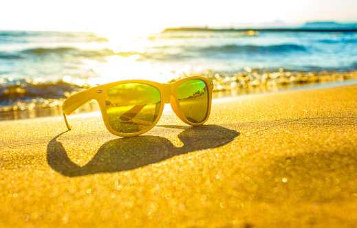 stylish yellow sunglasses on the yellow sand of the sea shore against the bright sun. the concept of a beach holiday at the sea.