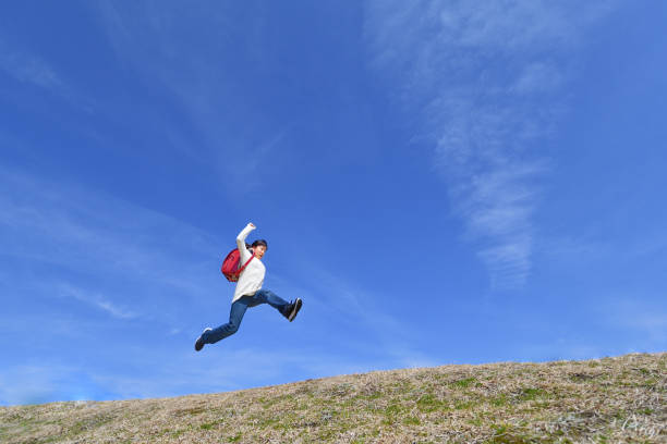 istock Japanese elementary school girl jumping in the blue sky 1146245675
