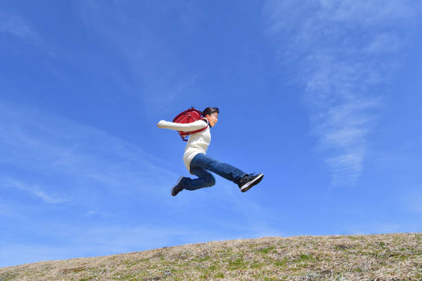 istock Japanese elementary school girl jumping in the blue sky 1146246248