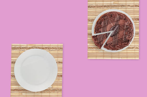 istock One cuted chocolate cake with cream and leaf on white ceramic round plate and bamboo rug on pink table in kitchen. Top view 1146249337