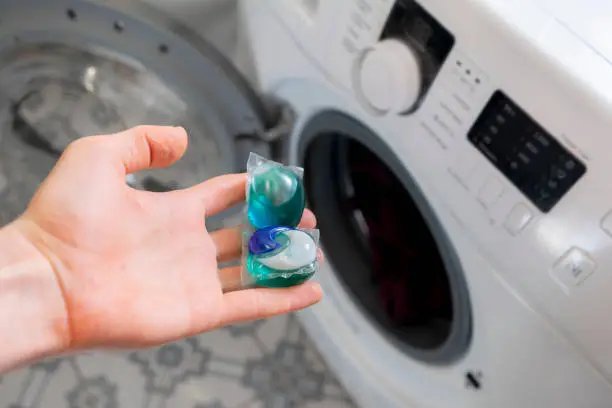 persons hand put special cleaning pod or capsule in the washing machine with dirty clothes