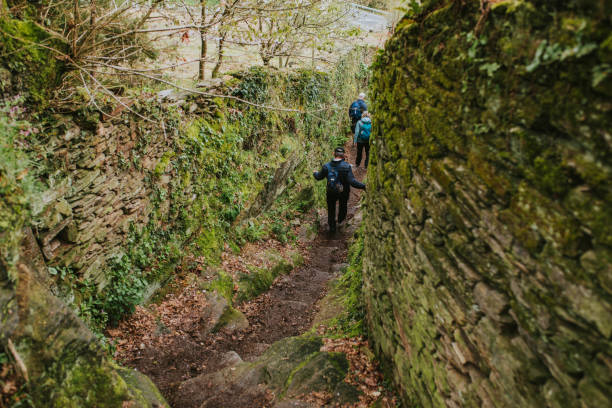 gruppo di persone che attraversano uno stretto sentiero in un ambiente verde durante il percorso escursionistico del camino de santiago. - portomarin foto e immagini stock