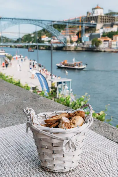 Selective focus of rustic basket full of different types of bread overlooking Cais da Ribeira and Ponte de Dom Luis I on the River Douro in Porto, Portugal