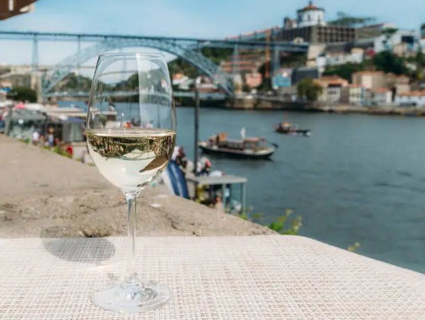 Selective focus of white wine glass overlooking Cais da Ribeira and Ponte de Dom Luis I on the River Douro in Porto, Portugal - reflection of bridge on glass
