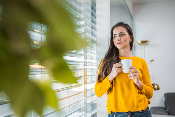 istock Beautiful brown haired woman drinking coffee and standing by a window 1146253661