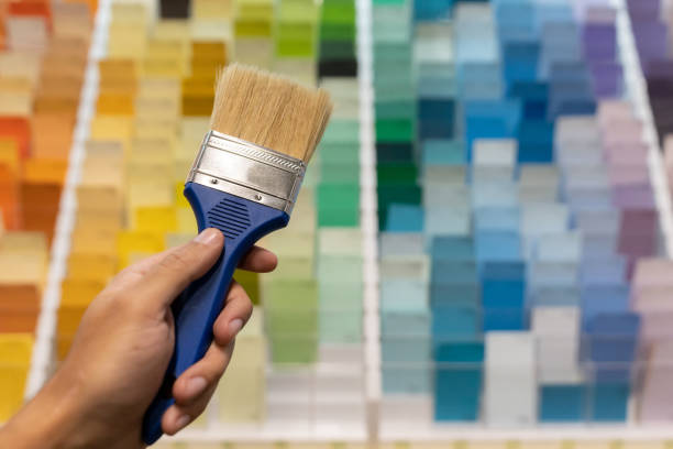 Happy Asian young woman looking at the color palette and comparing against the color on a concrete wall. Home DIY concept.