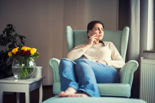 Woman speaks on the phone at home, she looking sad A young woman frowning as she speaks on the phone one young woman only stock pictures, royalty-free photos & images