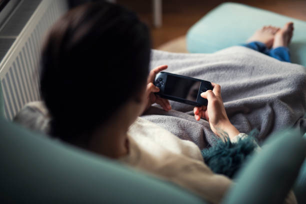 Young woman playing portable game at home. Young Latino woman playing portable games at home. handheld video game stock pictures, royalty-free photos & images