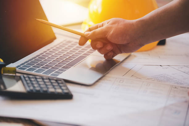 istock Hand holding pencil pointing on screen laptop architect tools on paper white plan building construction,Concept work architect 1146259645