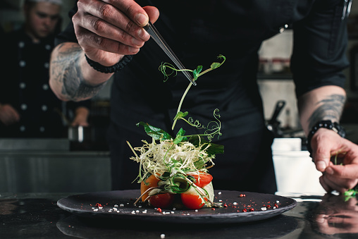 Chef terminando una ensalada sana en un plato negro con pinzas. casi listo para servirlo en una mesa photo