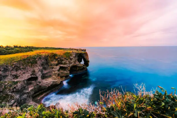 Photo of Manzamo or Manza cape, the landmark cape in Okinawa,Japan during dusk. The sky is orange and blue.