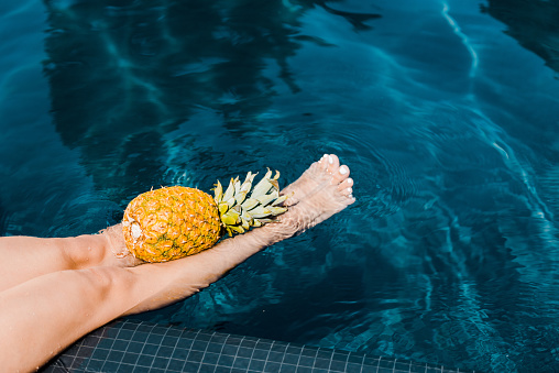 low section view of girl posing with fresh pineapple near swimming pool