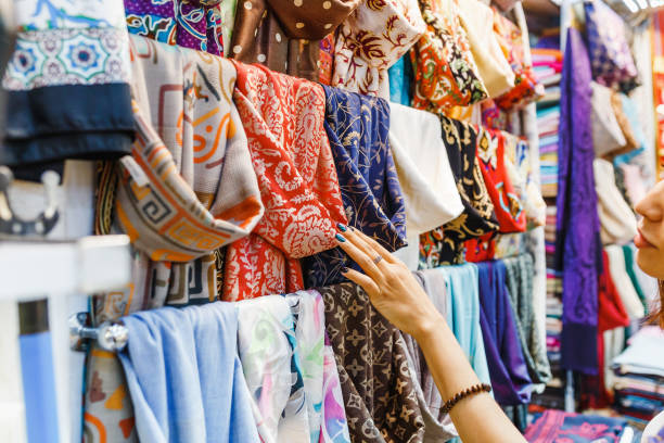 young woman shopping for a new scarf and choosing colorful fabric in bazar - merchandise multi colored arrangement blue imagens e fotografias de stock