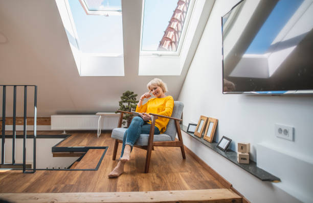 Senior Woman Enjoying Alone Time With Her Digital Tablet in a Cozy Nook Senior woman relaxing with her digital tablet in a sky-lit cozy nook. nook architecture photos stock pictures, royalty-free photos & images