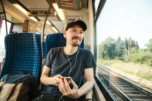 A young man listens to a music or podcast and looks out the window while the train is moving.