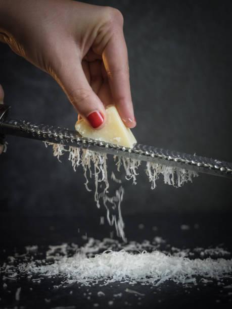 Hand of a woman grating parmesan cheese on a black background. Dark food. Italian cheese Parmigiano Reggiano stock photo