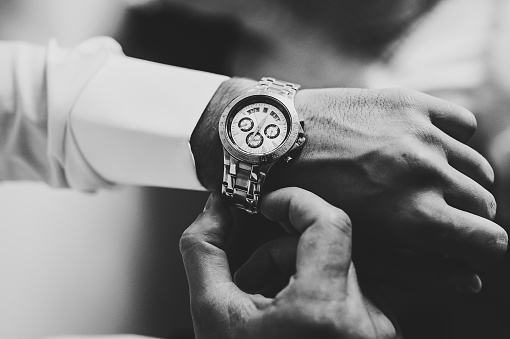 Black and white photo, man in a shirt adjusts the watch on his arm. Close up of businessman using watch.