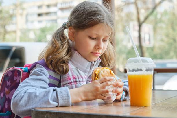 outdoor-porträt hübsche schülerin 8,9 jahre alt mit cheeseburger und orangensaft, fast-food-restaurant hintergrund - children only photography drink 8 9 years stock-fotos und bilder