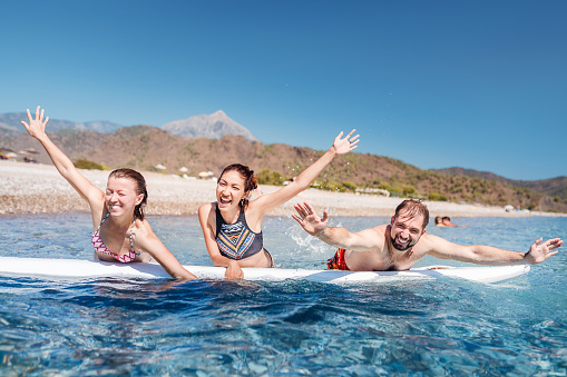 A multinational group of three friends of students laugh and swim in the sea with a board near the beach. Concept of travel and friendship