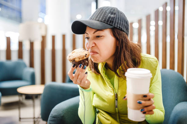 A woman in a fast food cafe with muffin and coffee in her hands smelling spoiled food A woman in a fast food cafe with muffin and coffee in her hands smelling spoiled food biscuit quick bread photos stock pictures, royalty-free photos & images