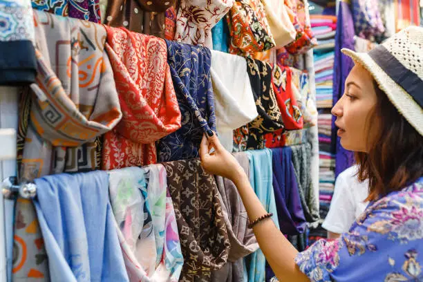 Photo of Young Woman Shopping For A New Scarf and choosing colorful fabric in bazar