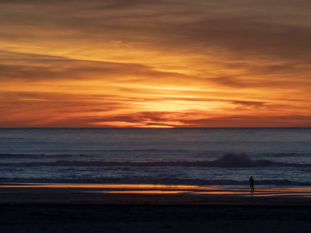 istock Man watches waves over ocean with sun setting during dusk hours 1146301676