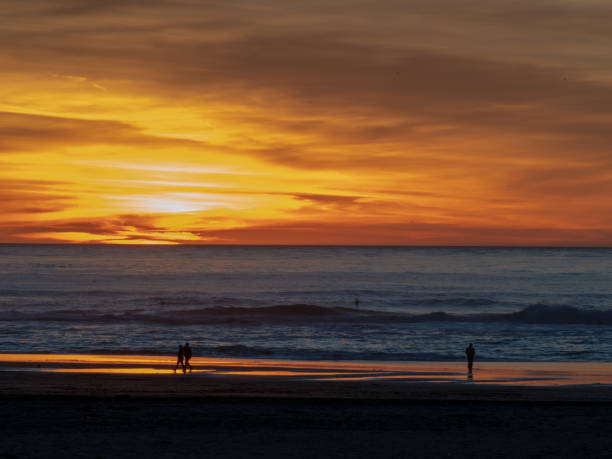 istock Sunset during dusk over Pacific Ocean with couples, surfers, and walkers 1146301709