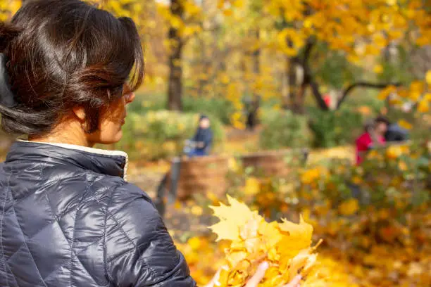 A woman looks at the yellow fallen leaves. Walk in the park on a sunny autumn day in a good mood.