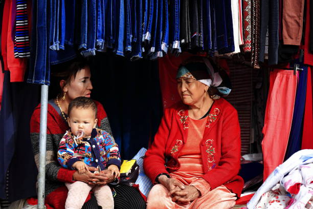 nonna-madre-nipote chiacchierando in una bancarella che vende vestiti per bambini-hotan sunday market-xinjiang-china-0103 - uighur foto e immagini stock