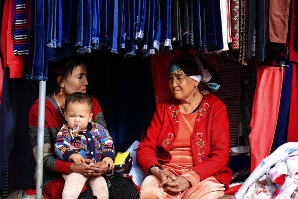 avó-mãe-neto que conversa em uma tenda que vende a roupa das crianças-mercado de domingo de hotan-xinjiang-china-0103 - cultura uigur - fotografias e filmes do acervo