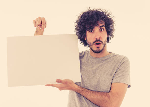 istock Funny and good looking millennial man showing and pointing at blank board with copy space for advertisement text. Looking happy surprised and shocked at great ad. In marketing concept. 1146318659