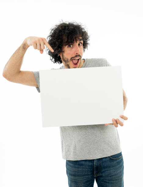 istock Funny and good looking millennial man showing and pointing at blank board with copy space for text. Friendly and excited young stylish man holding blank poster for advertisement. In marketing concept. 1146318697