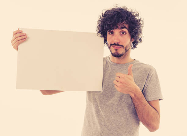 istock Funny and good looking millennial man showing and pointing at blank board with copy space for text. Friendly and excited young stylish man holding blank poster for advertisement. In marketing concept. 1146318707