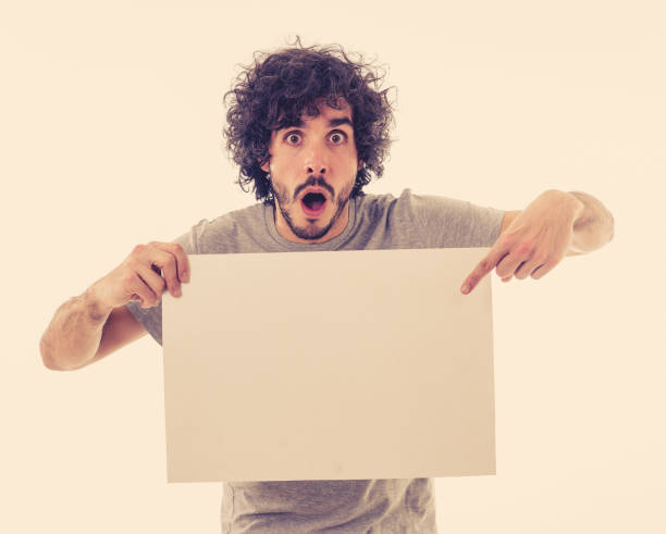 istock Funny and attractive millennial man showing blank poster with copy space for text looking excited as it shows a great product or amazing sale or great advertisement. studio shot. Marketing concept. 1146318781