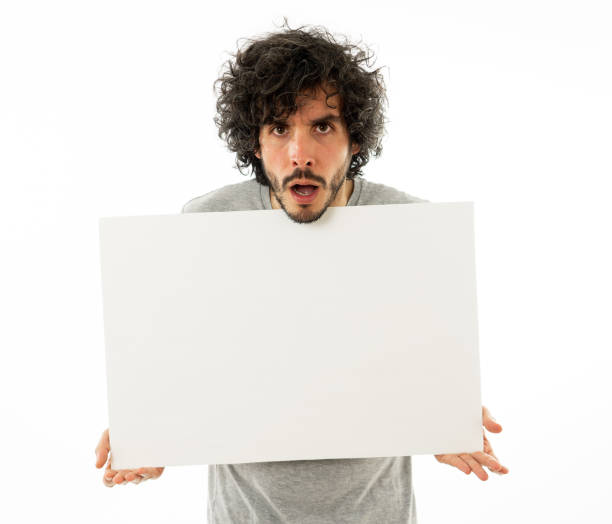 istock Funny and good looking millennial man showing and pointing at blank board with copy space for advertisement text. Looking happy surprised and shocked at great ad. In marketing concept. 1146319576