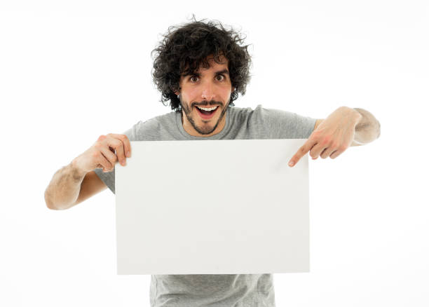 istock Funny and attractive millennial man showing blank poster with copy space for text looking excited as it shows a great product or amazing sale or great advertisement. studio shot. Marketing concept. 1146319680