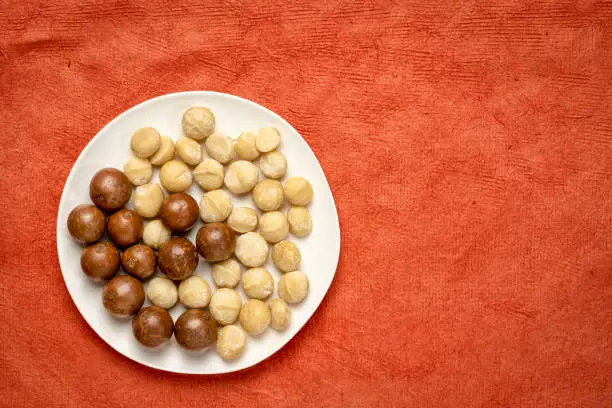 macadamia nuts on a white plate against red textured paper with a copy space