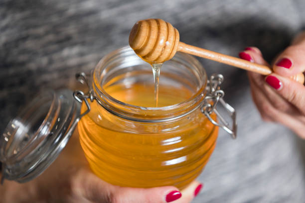 mujer sosteniendo frasco de vidrio de miel - honey fotografías e imágenes de stock