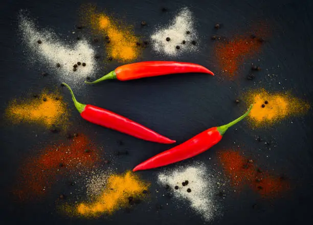 Hot pepper seasoning on dark slate background. Red chili peppers, black peppercorns, and pepper powder.
