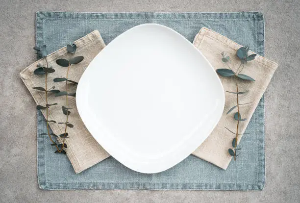 Elegant table setting decorated with eucalyptus branches. White plate and linen napkins.